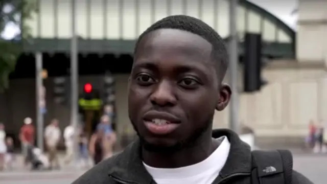 Headshot of a man standing in a street. He is talking as he looks off to the side of the camera