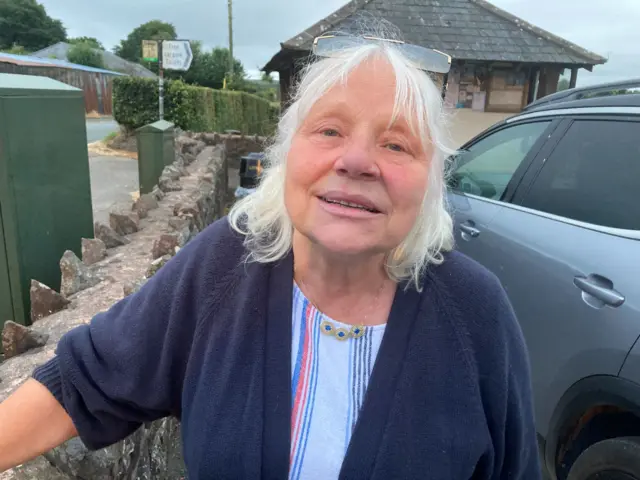 Wheddon Cross resident Jill looks at the camera. She has white hair and is wearing a blue cardigan over a white top with colourful stripes on it