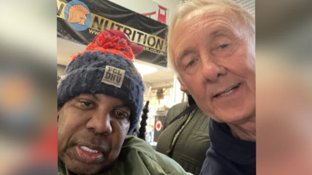 David 'Syd' Lawrence and Andy Brassington. David 'Syd' Lawrence is on the left of the frame wearing a blue and red bobble hat. Andy Brassington is next to him. He has short white hair and is leaning in towards Mr Lawrence, looking at the camera and smiling.