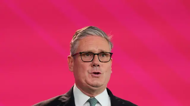 Close up of Keir Starmer in black suit in front of red background wall