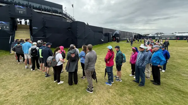 A queue of people snakes around the first grandstand