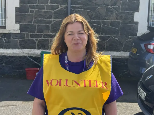 a woman with a big smile wearing a bright yellow tabard with the word VOLUNTEER on it