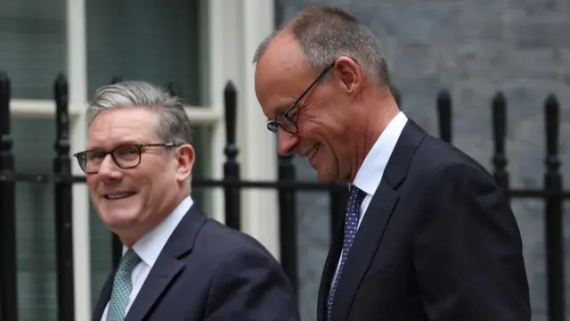 Merz looks down smiling as he walks towards Downing St alongside Starmer