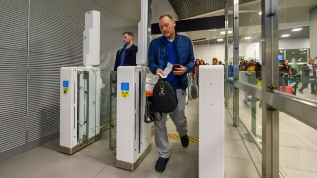 A man in a blue jacket carries a black bag through an e-gate at Lisbon airport.