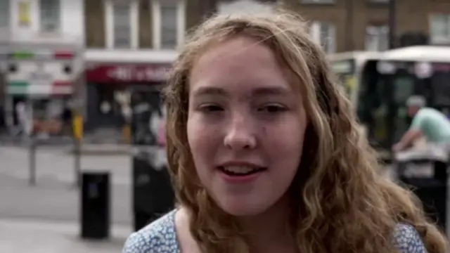 A woman speaking and looking to the side while she stands on a street