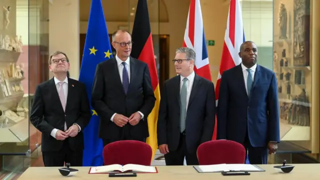 Starmer, Merz, Lammy and Wadephul stand in line, wearing suits, in front of flags of their respective countries.