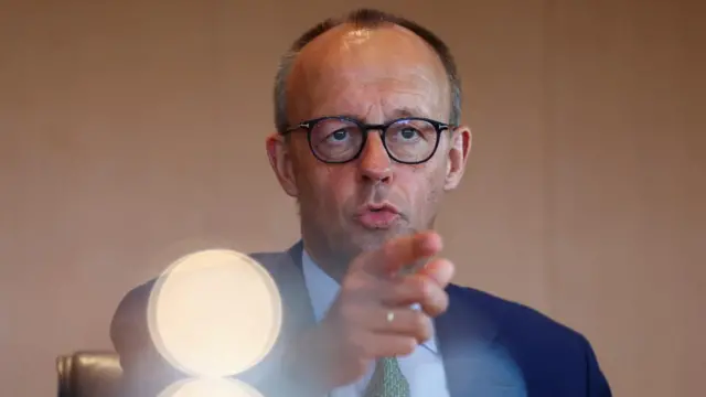 German Chancellor Friedrich Merz speaks wearing a suit and points.