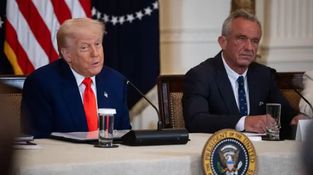 President Donald Trump and Health Secretary Robert F. Kennedy Jr. sit side by side at a desk taking part in a "Make America Healthy Again" event.