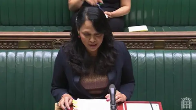 Democracy Minister Rushanara Ali in black blazer and brown top delivers speech from the despatch box inside the House of Commons, green leather and wooden benches behind her
