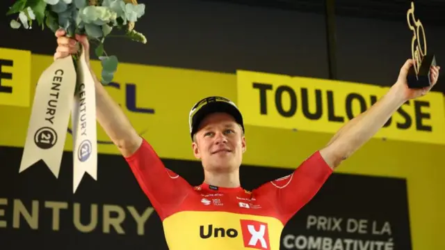 Jonas Abrahamsen with his arms aloft on the podium after winning stage 11 of the 2025 Tour de France