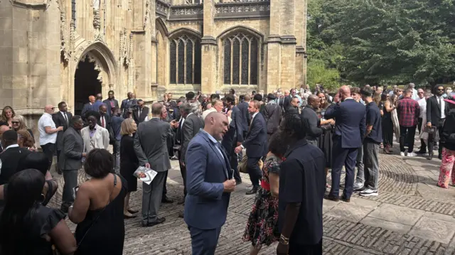Hundreds of people gathered outside the church in Bristol. Most are huddled in groups talking and wearing black.