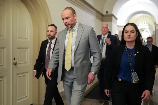 Dan Bongino, wearing a light grey suit, check shirt and yellow tie, walks in the US Capitol alongside others.