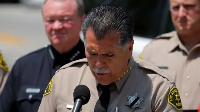 A man in a sheriff's uniform speaks from a podium