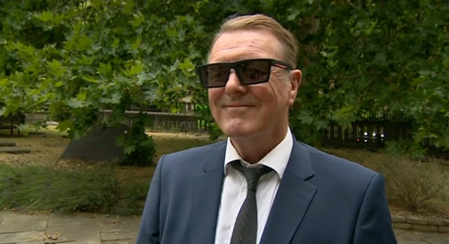 Phil Tufnell outside the church in Bristol for the funeral. He is wearing a suit, with a black tie.