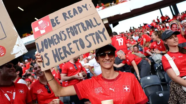 A fan of Switzerland holds up a sign reading "be ready: women's football is here to stay"