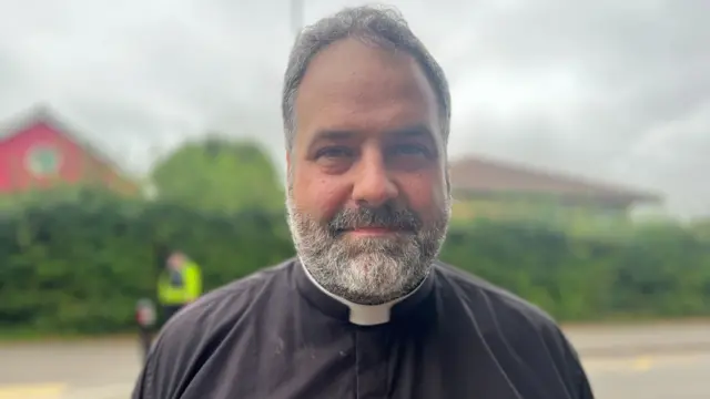 Reverend Philip Butcher stood outside Minehead Middle School. He is dressed in all black.