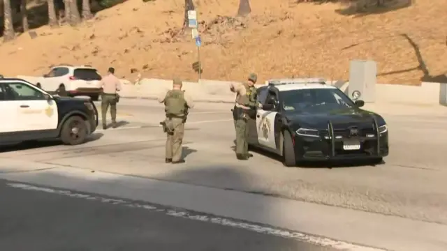 An officer at a police cordon gives directions to a colleague in a black and white sheriff's car