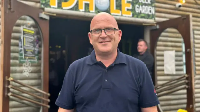 Adrian Calvin, he is looking into the camera and smiling. He is wearing a navy polo and glasses.