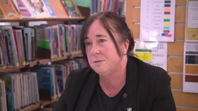 Laura Mackie, wearing all black. She has dark hair and is sitting in what looks like a school library.