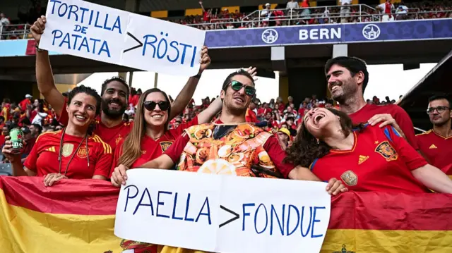 Spanish supporters hold signs about Spanish and swiss food