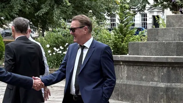 Phil Tufnell outside the church in Bristol. He is shaking hands with someone, who is not pictured.