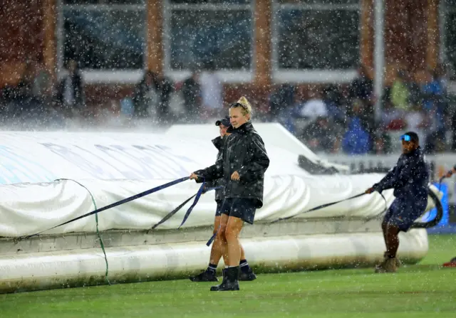 Ground staff bringing on the covers