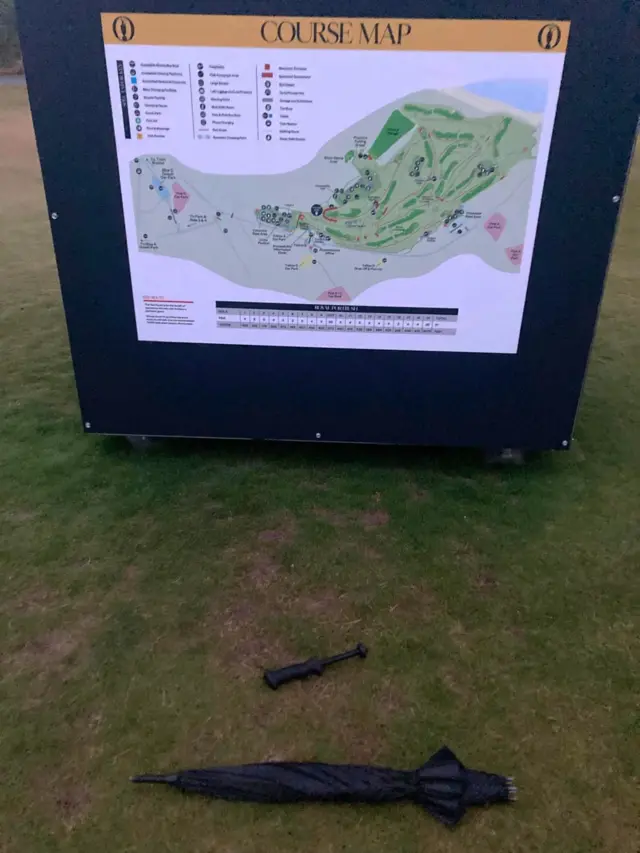 A picture of a broken umbrella in front of a course map sign
