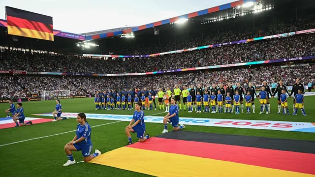 France's players kneel down next to France's (L) and Germany's national flags displayed on the pitch