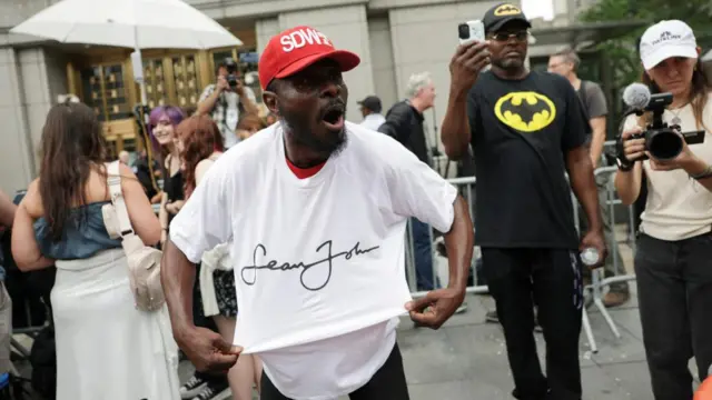 A man in a white t-shirt from Diddy's clothing brand and red cap yells