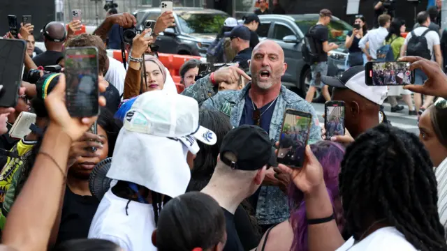 A bald man is shouting and people are filming them on his phone