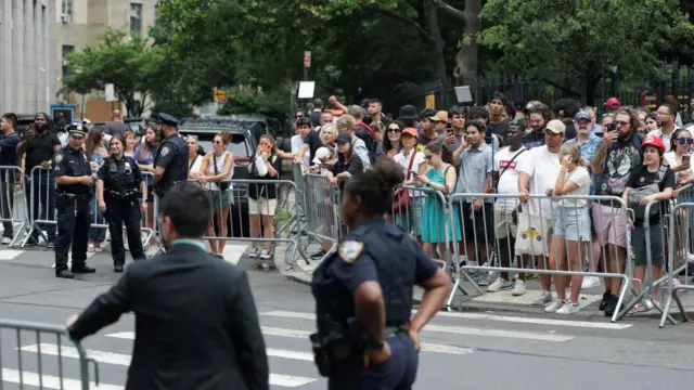 A closed off street with people stood behind the barriers and police watching them