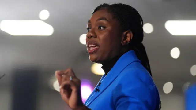 kemi badenoch gestures. she is wearing a blue blazer.
