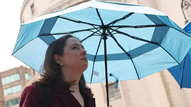 A woman walking with an umbrella that is blue