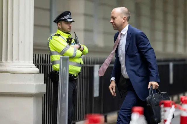 Hancock walking into the Covid inquiry holding a briefcase as a police man stands outside