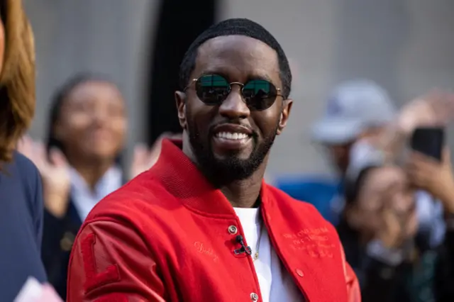 Diddy wearing a red jacket over a white shirt. He is is wearing black sunglasses in this 2023 photo