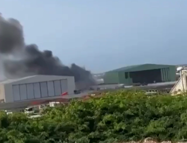Still taken from a video circulating on social media showing a plume of black smoke between two aircraft hangers