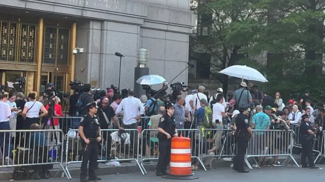 A crowd of people behind barriers, which are lined by police officers