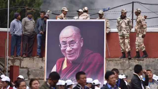 Indian security personnel stand beside a poster of exiled Tibetan spiritual leader the Dalai Lama as he delivers religious teachings at the Buddha Stadium in Bomdila in India's north-eastern state of Arunachal Pradesh state on April 5, 2017
