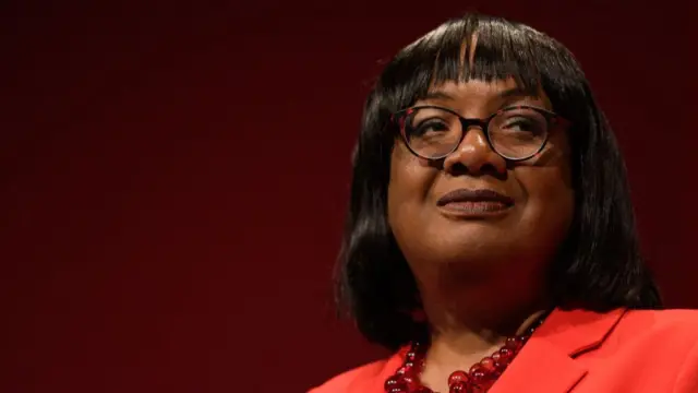 Close up of suspended Labour MP Diane Abbott wears a bright red blazer, against a dark red background.