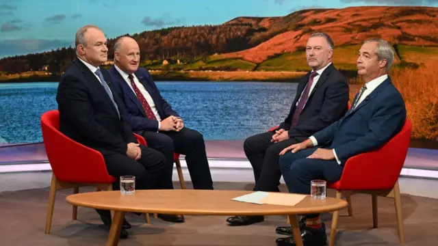 The four guests, all in suits, sit facing each other in red chairs but not looking at one another on the BBC TV set