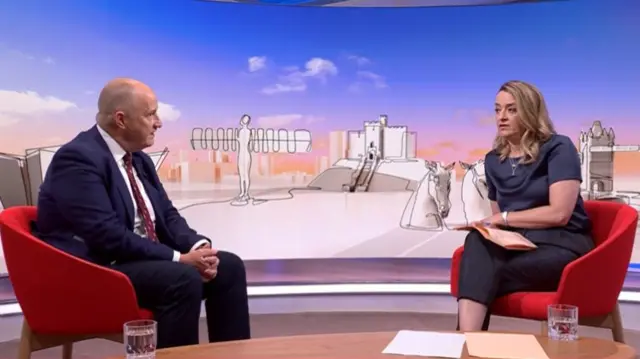 Kevin Hollinrake (L) sits down in a red chair wearing a dark blue suit as he listens to Laura Kuenssberg (R) asking him questions from a matching chair