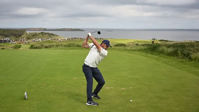 A wide image of Bryson DeChambeau teeing off at the fifth