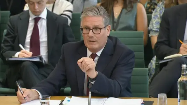 Keir Starmer appears before the Liaison Committee. He points with his hand in the direction of the person asking a question and has a serene expression.
