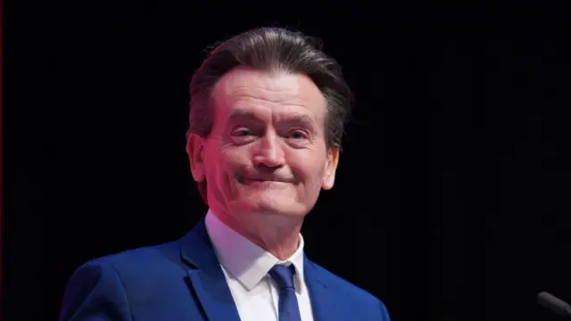 Feargal Sharkey smiling at the camera, wearing a blue suit and tie