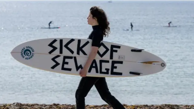 A Surfers Against Sewage protest in Falmouth last year, with a woman holding a surfboard saying "sick of sewage"