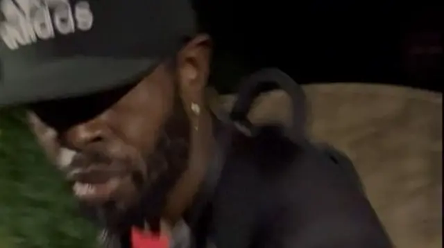 A man pictured wearing a black cap and a black jacket, he has a beard.