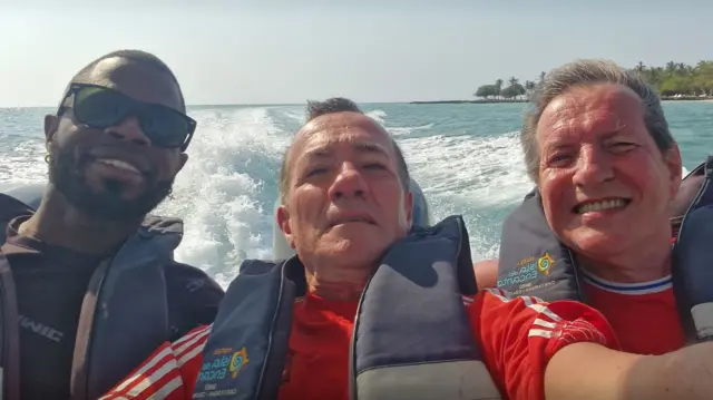 Three men looking at a camera while on a speed boat ride in a holiday resort.