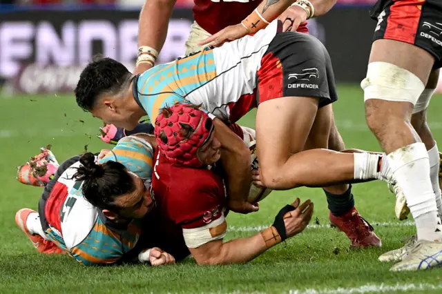 First Nations & Pasifika XV players Andy Muirhead (L) and Kalani Thomas (R) tackle British and Irish Lions' Josh van der Flier