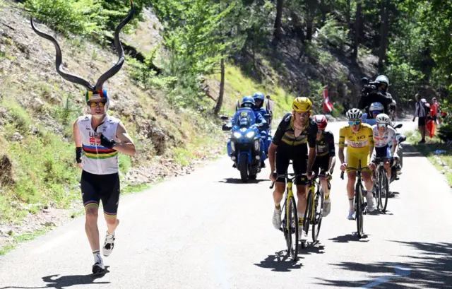 A UAE Emirates fan wearing a helmet with huge horns as Tour de France riders go past during stage 16 of the 2025 race