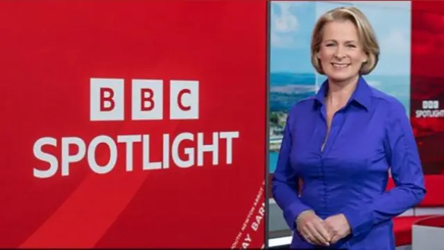 Victoria Graham is smiling as she stands next to a screen that reads BBC Spotlight. She is wearing a blue blouse and has a blonde bob.